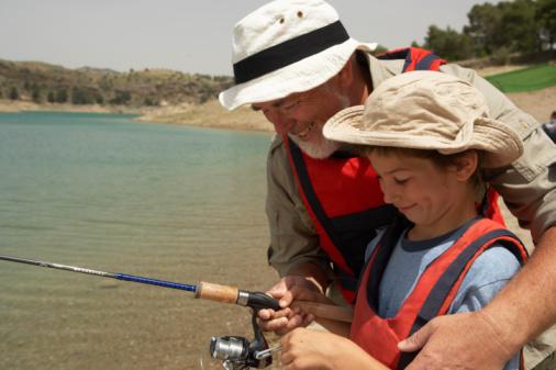 Grandfather teaching grandson (5-7) to fish, smiling, close-up
