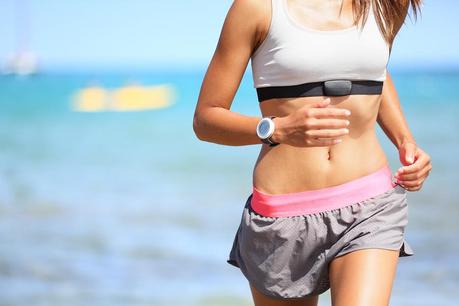 Runner woman with heart rate monitor running on beach with watch