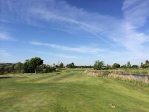 Palomarejos Golf – Derby Madridistas Colchoneros Salida del 15, con la ria que cruza la calle (al fondo)