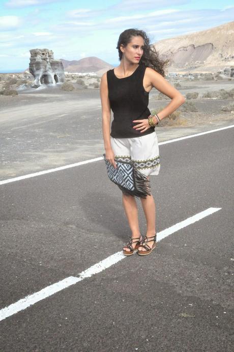 estoy situada en medio de la carretera al lado de la rofera en Teseguite (Lanzarote), con una falda color crema, camiseta negra y cuñas negras abiertas