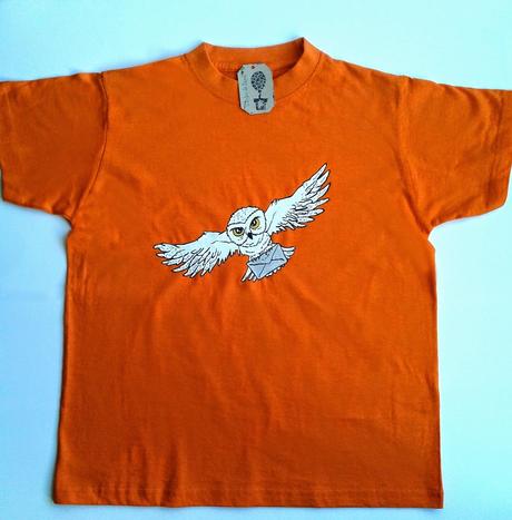 Camiseta naranja para niño o niña pintada a mano con la lechuza blanca de Harry Potter. Tiene las alas extendidas y lleva en las garras un sobre.