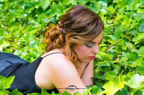 Chica posando tumbada entre yerba verde con peinado rizos y maquillaje de fiesta 