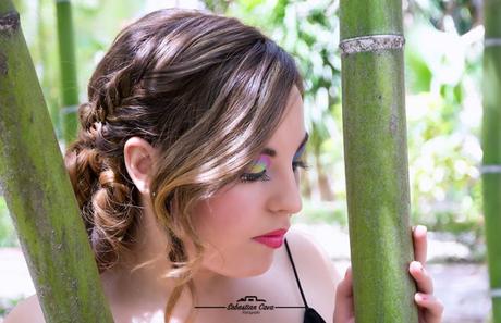 Chica posando entre bambu con peinado de rizos y maquillaje de fiesta