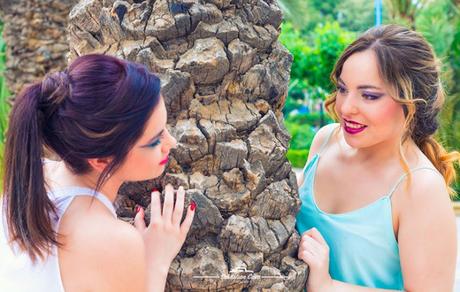Peinados Y Maquillaje Para Peluquería Dual Dos chicas posando junto a palmera mirándose con maquillajes de fiesta y peinados elaborados