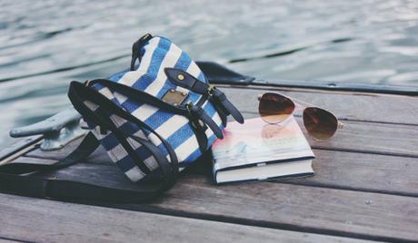 Bolso, libro y gafas de sol apoyadas en un muelle junto al mar.