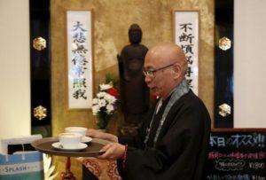Shokyo Miura, a Buddhist monk and one of the on-site priests, carries cups of coffee past a statue of Buddha at Tera Cafe in Tokyo, Japan, April 1, 2016. REUTERS/Yuya Shino