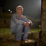 Senior man in pyjamas sitting outside house at night