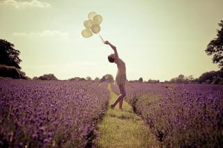 Mujer joven jugando con globos de colores en un camino que divide un campo de lilas.