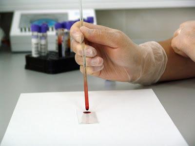 La imagen muestra un laboratorio en el que un analista trabaja con una muestra de sangre. Al fondo se ven más tubos con muestras