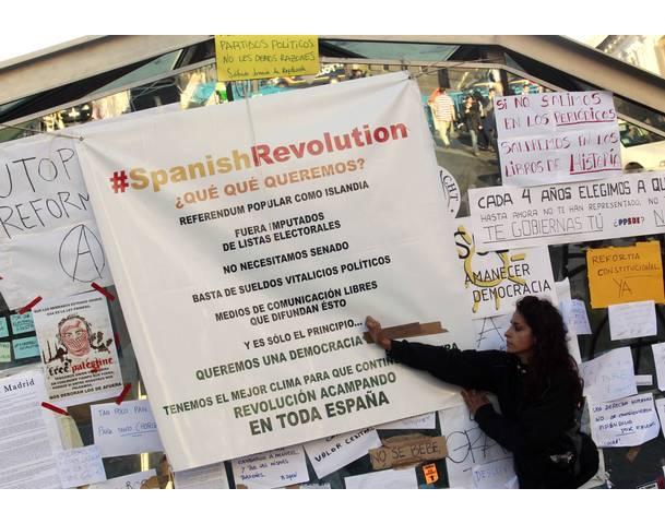 DEMOCRACIA REAL, YA! A demonstrator puts a sticker on a poster at Madrid's famous landmark Puerta del Sol