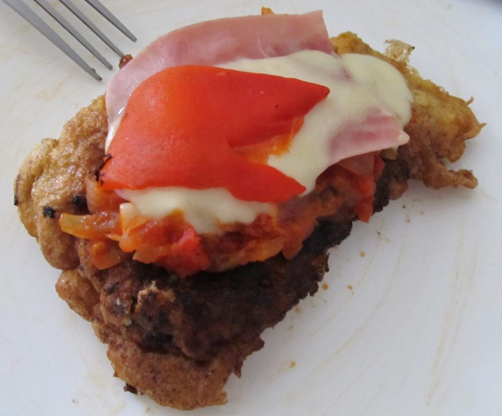 Ternera gallega empanizada, frita en muy poco aceite de oliva, luego al horno con salsa de tomate, cebollas y ajo, y su porción de jamón, pimiento rojo morrón y mozarella