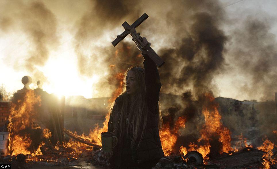KEEPING THE FAITH: An Irish traveler resident holds up a cross for the media, in front of a burning barricade during evictions at the Dale Farm travellers site, near Basildon 