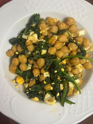 Un plato hondo de cerĂĄmica blanca con relieve, lleno de garbanzos salteados con espinacas cocinadas y trozos de huevo duro picado.
