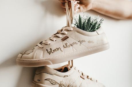 Mujer sosteniendo unos zapatos deportivos por los cordones con flores en su interior Mujer sosteniendo unos zapatos deportivos por los cordones con flores en su interior