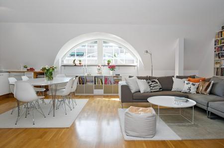 ventana redondeada suelo de parquet sofá gris sillas eames muebles blancos decoración limpieza en ático diáfano estilo nórdico estilo escandinavo electrodomésticos silenciosos decorar pisos decorar con muebles de ikea decoración estilo nórdico decoración escandinava decoración diáfana decoración de áticos cocina blanca blog deco blog de interiorismo blog de decoración ático diáfano 