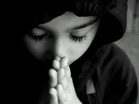 Foto de un niño en actitud reverente, sus ojos están cerrados, cabeza inclinada y las manos juntas para orar.