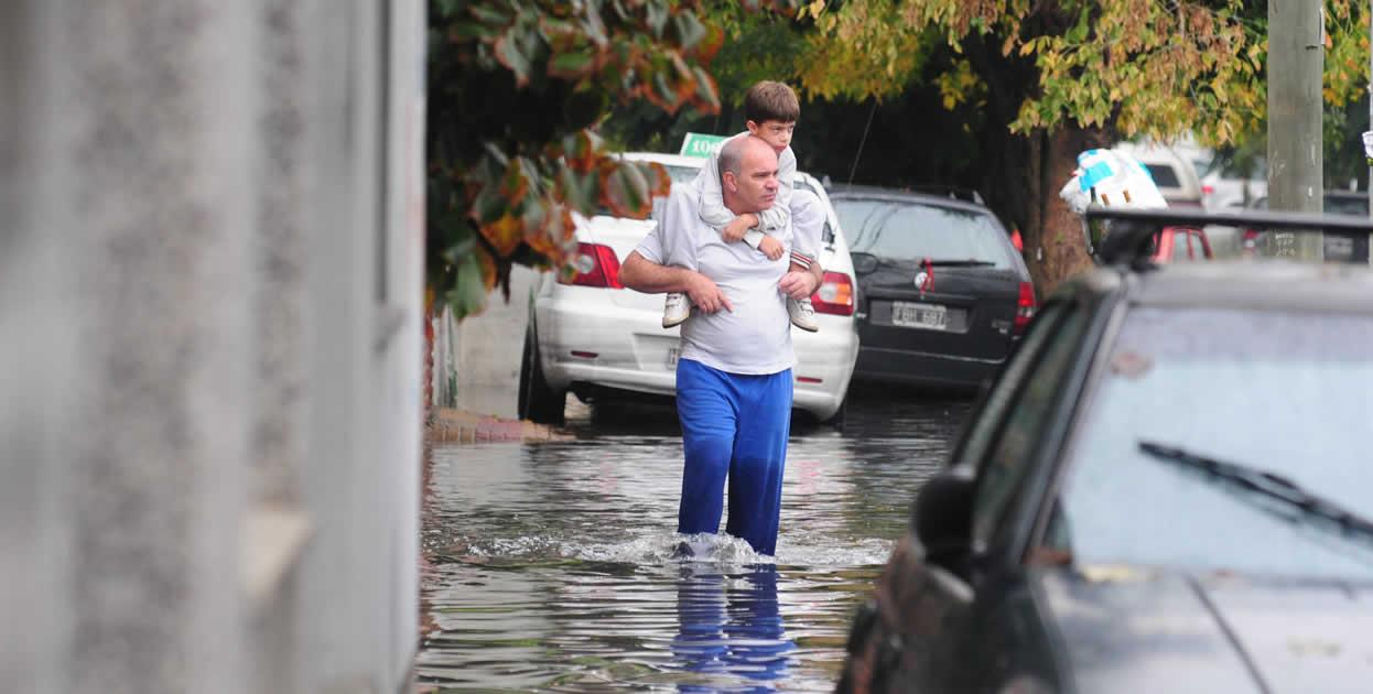 Un hombre sostiene a un niño mientras camina por una calle inundada. EFE/Javier Brusco