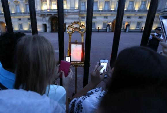 People take pictures of a notice proclaiming the birth of a baby boy to Prince William and Kate, Duchess of Cambridge on display for public view at Buckingham Palace in London, Monday, July 22, 2013.