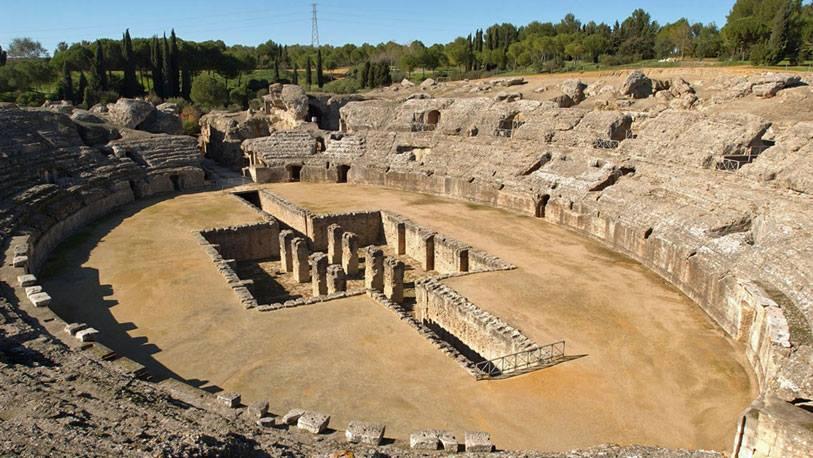 Foto: -ITÁLICA, ESPEJO DE ROMA-  A pocos kilómetros de Sevilla, a un lado del viejo río Guadalquivir, duermen las ruinas de Itálica, uno de los conjuntos arqueológicos de época romana más importantes de España. Aquí nacieron los emperadores Trajano y Adriano, enaltecidos por la pluma de la escritora francesa Marguerite Yourcenar.  Las casas patricias, el teatro y el anfiteatro, el circo donde combatieron las fieras, las calles pavimentadas y los grandes foros donde un día se levantaron los grandes monumentos de la administración guardan un eco lejano en este singular mundo de ruinas y piedras reconstruidas. Visitar Itálica es una invitación a vestir con toga romana. La historia la sitúa entre las grandes ciudades de la república, y sobre todo, del imperio.  -La fundación-  Itálica fue fundada por Escipión el Africano en el año 206 antes de Cristo, tras vencer a los cartagineses en la batalla de Ilipa. Los rastros que han llegado hasta nuestros días demuestran que Itálica fue una ciudad palatina levantada para el descanso. En cambio, la vecina Hispalis era la urbe comercial y portuaria. Los patricios llegaban a ella para vigilar sus negocios y rubricar acuerdos. En Itálica les esperaba el descanso.  Hoy sabemos que la ciudad estaba ordenada como un tablero de ajedrez y que las fachadas de las casas estaban decoradas con mármoles traídos de Italia, Grecia y el mítico Oriente. De todo aquello sólo queda un esqueleto de piedra. No hay jaspes, ni mármoles, ni mosaicos algunos. Una mínima parte de todo aquello está repartido por varios museos.  Itálica es ahora un conjunto de ecos inmóviles y exánimes. Por sus calzadas pasean historiadores y curiosos de las intimidades del semejante que buscan en el interior de las casas descubiertas alguna muestra de la vida que aquí dejaron sus moradores. Los huesos de Itálica reposan en un amable juego de colinas y lomas, al lado de Santiponce.   A seis kilómetros está el río Guadalquivir donde desembarcaban las riquezas que durante largo tiempo colmó de lindas apariencias a esta ciudad. En el circo que entretenía las tardes de los potentados ciudadanos romanos no sacrificaban a animales exóticos. A la arena saltaban toros bravos, parientes muy lejanos de estos otros que hoy engrandecen la fiesta nacional.  -Lal casa y el anfiteatro-  A la entrada al conjunto arqueológico de Itálica se localiza una casa romana reconstruida. A pocos metros está el anfiteatro que en su día tuvo capacidad para más de 25.000 espectadores. Se cuenta que fue el tercero más importante en el antiguo mundo romano.  Asimismo, el teatro de Itálica se sitúa en una de las colinas que miran a la localidad de Santiponce. No lejos de aquí está el monasterio de San Isidoro del Campo, uno de los templos cristianos más importantes de la provincia de Sevilla. Itálica, además, es un hito importante dentro del llamado itinerario de la Vía de la Plata, que trepa hasta Extremadura y que tiene en la ciudad de Mérida una de sus más importantes paradas.  | Más información en www.museosdeandalucia.es y en www.turismosantiponce.es  Fuente: www.ocholeguas.com
