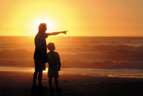 a father showing something to his son at sunset on a beach