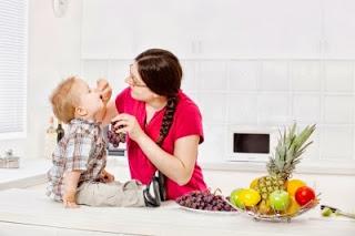madre dando de comer a su hijo fruta en la cocina