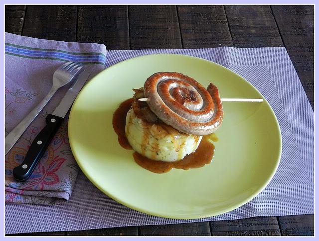 Piruleta de salchicha de ternera sobre timbal de patata y cebolla caramelizada