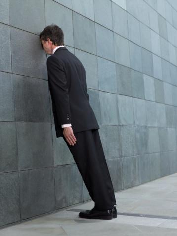 Businessman leaning forward, resting face against wall, side view