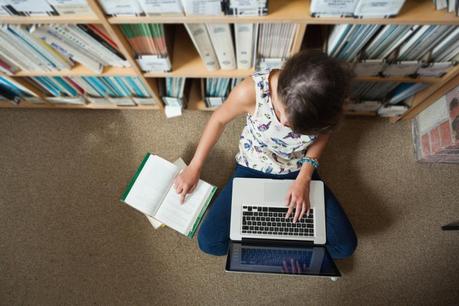 High angle view of a female student sitting against bookshelf 