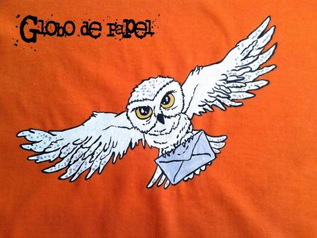 Detalle de la camiseta naranja para niño o niña pintada a mano con la lechuza blanca de Harry Potter. Tiene las alas extendidas y lleva en las garras un sobre.