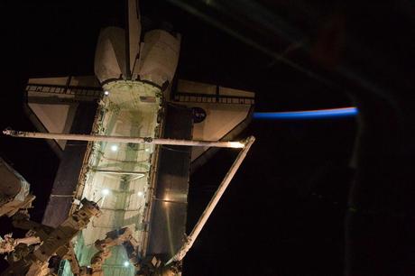 Shuttle Endeavour docked to the ISS, backdropped by a thinly lit part of Earth's atmosphere and the blackness of orbital nighttime in space