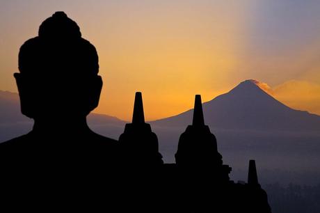 Silent Giants - A Buddha statue of the colossal temple of Borobudur overlooks the Merapi volcano at dawn. Both are silent and full of power
