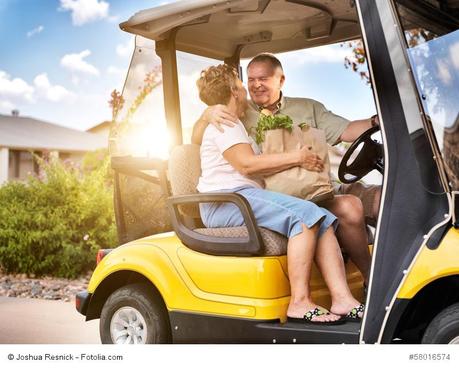 happy elderly couple coming home with groceries on golf cart