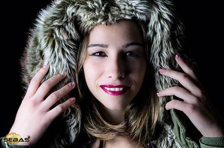 Chica modelo posando con gorro, maquillada y con uñas decoradas con fondo negro