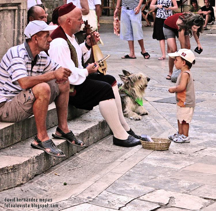 Un músico tradicional toca al lado de un perro y de otro hombre mientras un niño observa