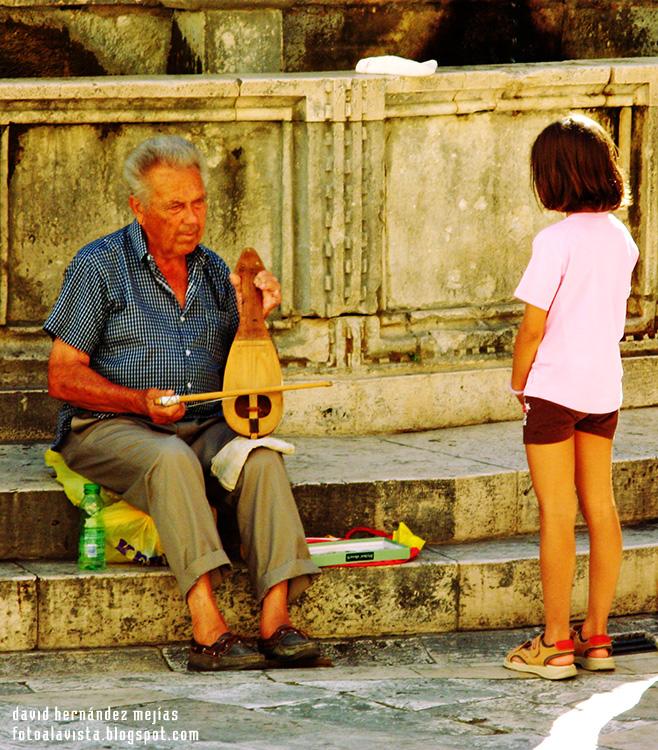 Un viejo músico toca un instrumento tradicional de cuerda mientras una niña observa