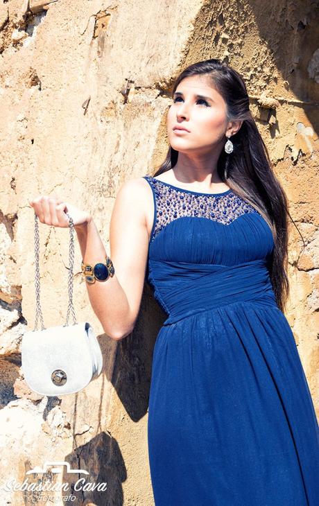 Modelo profesional con vestido azul y bolso blanco apoyada en pared