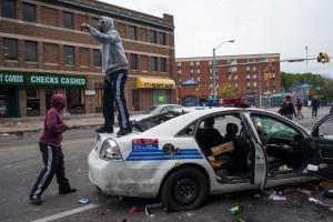 Varias personas gritan sobre un vehículo de la policía abandonado que fue atacado durante las protestastras el funeral de Freddie Gray. (EFE/NOAH SCIALOM) 