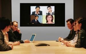 Businesspeople seated around conference table and monitor