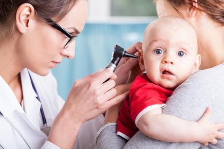 Young doctor examining baby boy with otoscope