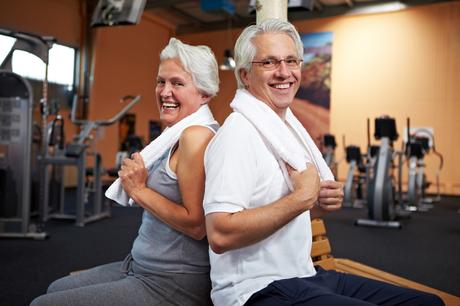 Lachendes Seniorenpaar im Fitnesscenter lehnt sich aneinander an