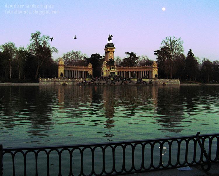 Vista atardeciendo del estanque y del monumento a Alfonso XII en el Parque del Buen Retiro de Madrid con la luna y dos patos volando