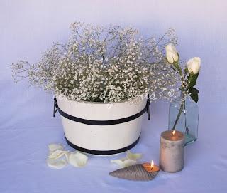 Bodegón con cubo de paniculata, recipientes de cristal con rosas y velas