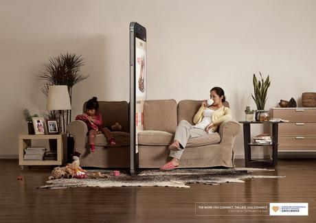 Mujer y una niña sentadas en un sillón separadas por un enorme celular 