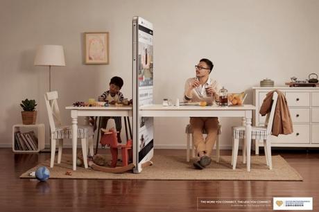 Hombre sentado a la mesa junto a su hijo separados por un celular 
