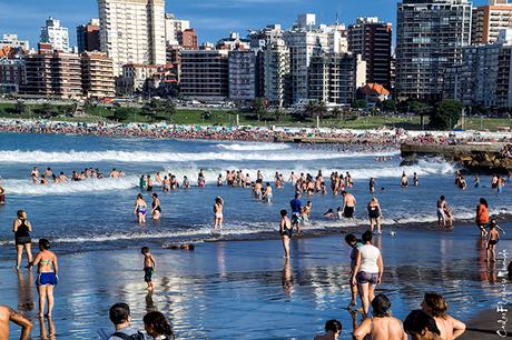 Playa con gente en el agua y la Ciudad de Mar del Plata al fondo.