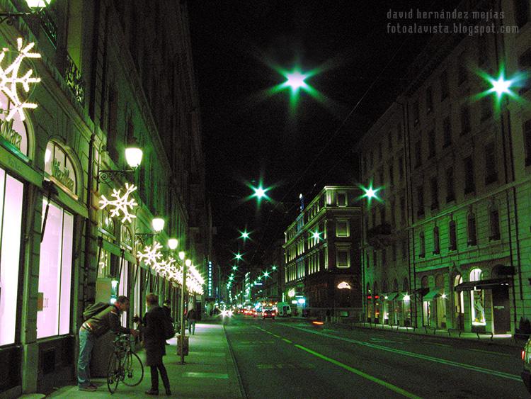 Calle de Ginebra iluminada por la noche en Navidad con una pareja en bicicleta que espera el autobús