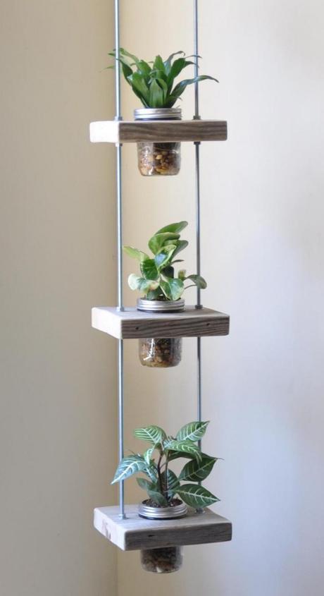 JARDÍN VERTICAL: ¿No tienes mucho espacio para lucir tus plantas favoritas? Don't worry! Sólo necesitas una esquina y algo de pericia: 1. Consigue algo de madera recuperada, varillas roscadas, tornillos y tarros de conserva con la parte superior más ancha que el centro. 2. Corta 4 piezas cuadradas de madera y hazles un agujero en el centro (que sean del tamaño de tus tarros) 3. Haz 2 agujeros en cada lado de la madera para poder pasar las varillas. 4. Introduce las arandelas y tornillos por encima y debajo de cada pieza de madera. Tendrás que ir alternándolos y colocándolos en la medida deseada. 5. Corta el centro de las tapaderas de los tarros, para que se vea un borde metálico y sirva además de soporte seguro. 6. Pon piedrecitas en el fondo de los tarros para que tus plantas puedan respirar. 7. Por último, cuelga este macetero del techo a la altura deseada usando cables de metal. Puedes poner tantas plantas como desees. Es una idea de Susie Frazier