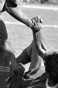 Un futbolista ayuda a otro a levantarse.