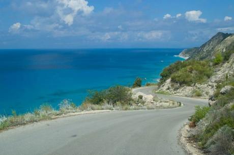 Carretera de descenso hacia la playa occidental de Lefkos, con el mar turquesa de fondo
