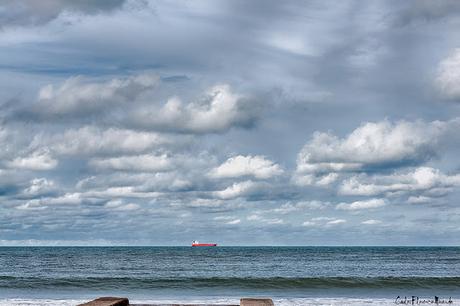 Paisaje nuboso con barco rojo en el horizonte.